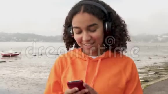 美丽的混血非裔美国少女在港口边散步用无线耳机听音乐视频的预览图