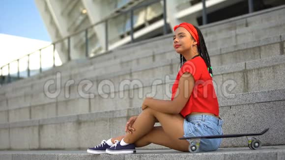 迷人的混血女孩与滑板休息户外等待朋友视频的预览图