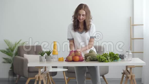 年轻可爱的女人准备做沙拉在舒适的厨房里桌子上有蔬菜和水果健康饮食视频的预览图