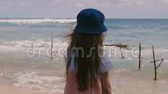 后景快乐的小女孩6岁至8岁留着长发戴着帽子看着异国情调的海滩上美丽的放松风景视频的预览图