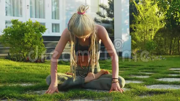 女人坐在房子后院的草坪上做腹部真空运动视频的预览图