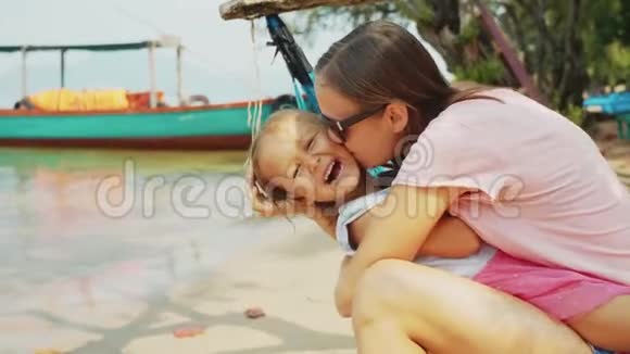 妈妈拥抱并亲吻她坐在沙滩吊床上的小女儿视频的预览图