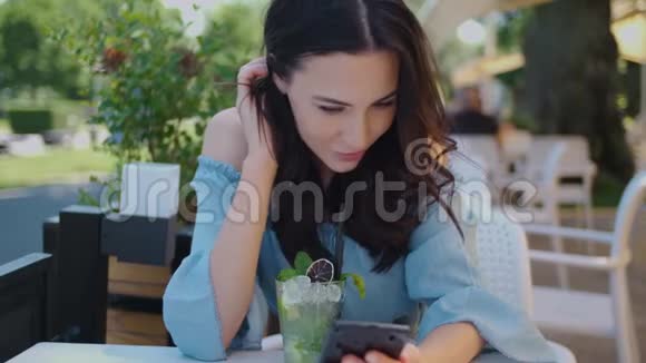 漂亮的黑发女人坐在户外餐馆用手机视频的预览图