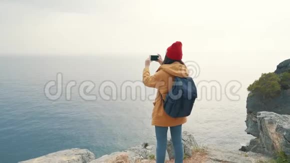 带背包的旅游女孩站在悬崖边上拍照视频的预览图
