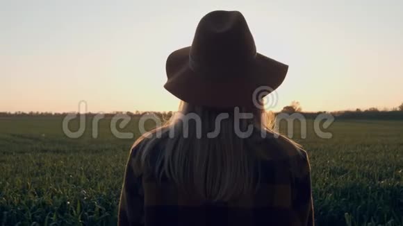 女孩用手看着太阳一个戴帽子的年轻女孩在日落或黎明时触摸太阳光绿色视频的预览图