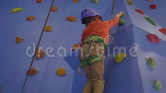 攀岩活动在人造攀岩墙上穿着马具的白种人男孩用抓地力爬墙视频的预览图