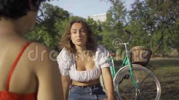 两个年轻的女人一边说话一边坐在夏天的花园里她们的自行车站在附近农村生活复古视频的预览图