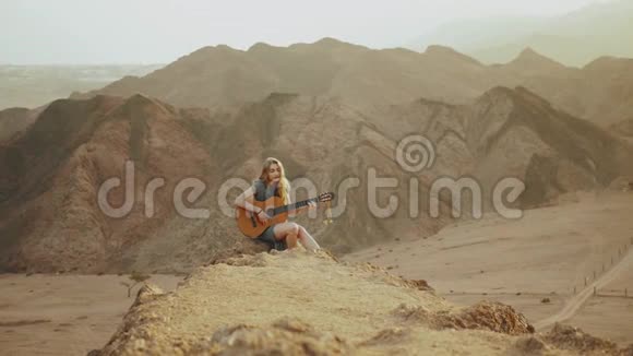 在沙漠风景沙漠山脉背景慢动作中弹吉他和唱歌的女性视频的预览图