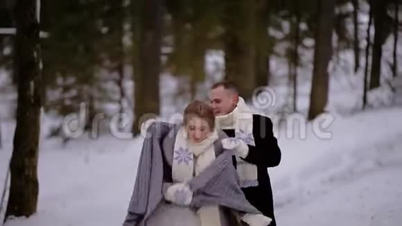 一对相爱的夫妇正穿过一片白雪皑皑的冬林情侣们戴着温暖的围巾一个年轻人照顾他的女孩视频的预览图
