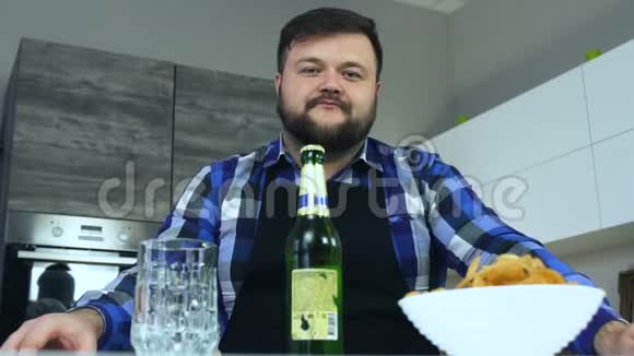 胖子坐在餐桌旁的厨房里用刀打开一瓶啤酒薯片在盘子里酒精视频的预览图