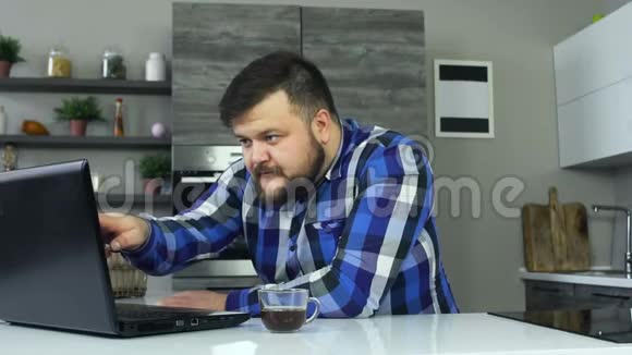 一个身材魁梧的家伙在笔记本电脑前的厨房里开始生气用手拍打桌子一个胖子视频的预览图
