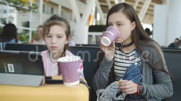 机场的小吃两个姐妹正在平板上看动画片用饼干喝茶视频的预览图