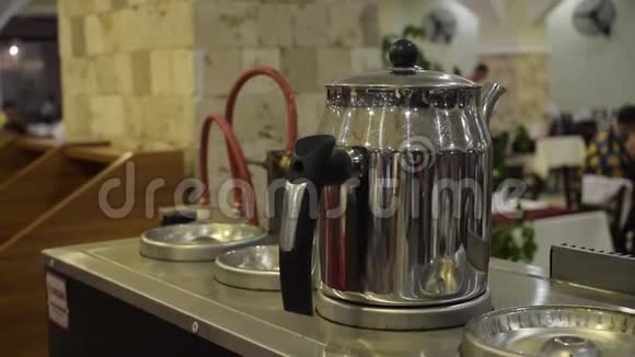在餐馆里人们拿着热而发亮的带黑色手柄的金属茶壶视频的预览图