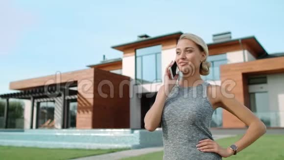 成功的女人在豪宅附近说话移动快乐女人打电话视频的预览图