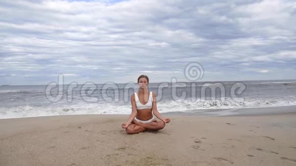 年轻女子正在海滩上慢动作练习莲花姿势瑜伽视频的预览图