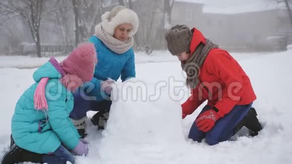 父母和孩子在雪地里玩耍妈妈和两个女儿在冬天堆雪人视频的预览图
