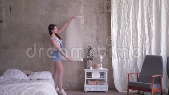 微笑女主人的肖像她拿着一卷新墙纸靠近空墙然后在装修期间看镜头视频的预览图