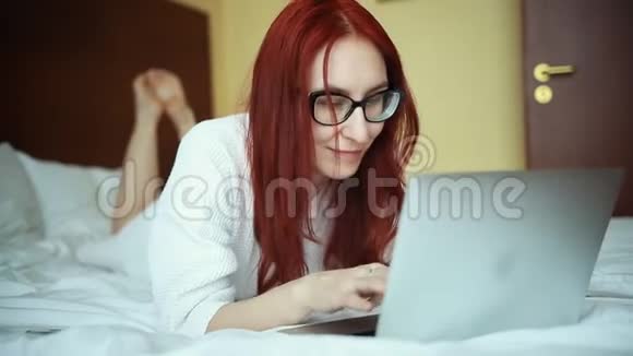 一个穿浴袍的姜女躺在床上拿着笔记本电脑工作自由职业视频的预览图