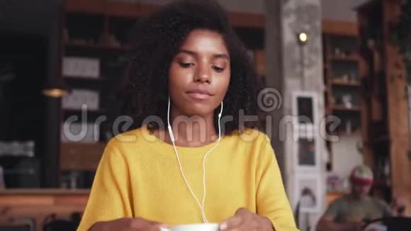 年轻女子拿着一杯咖啡用耳机听音乐视频的预览图