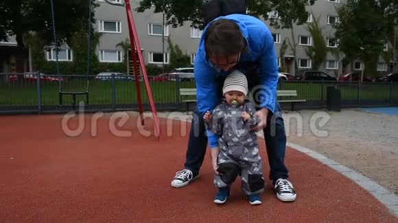 父亲牵着婴儿的手帮助他走路视频的预览图