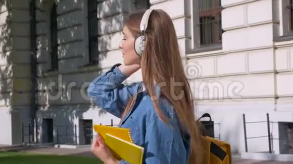 快乐的金发女孩微笑着手里拿着笔记本用耳机听音乐反对的意见视频的预览图