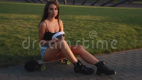 年轻的滑板女郎坐着戴上耳机视频的预览图