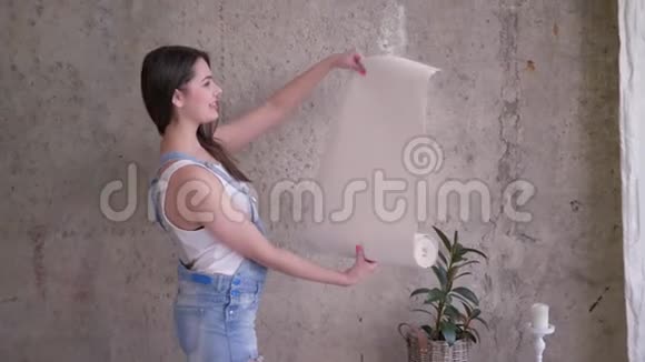 公寓的新主人女人的肖像在室内的空墙附近修理和拿着一卷壁纸视频的预览图