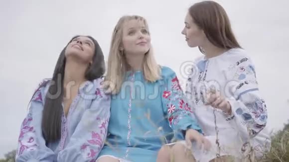 三位身穿夏季时装长裙的年轻女友在赛场上交谈两个高加索女孩和一个非洲女孩视频的预览图