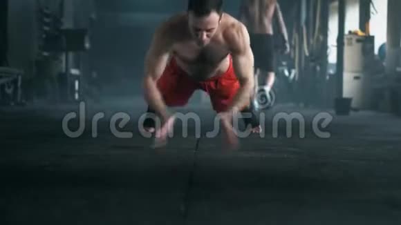 一个拥有美丽身体和赤裸躯干的运动员在体育馆的地板上做俯卧撑4K暗色调拍摄视频的预览图