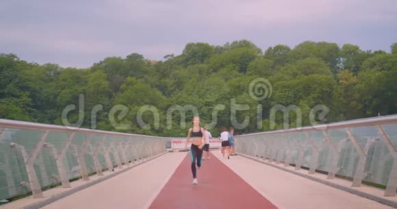 城市户外桥上跑步的年轻漂亮运动女性慢跑者的近景前景视频的预览图