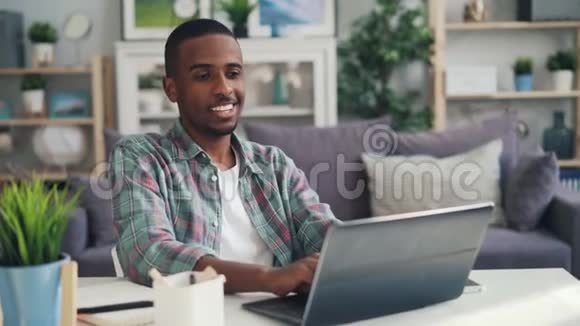 一个快乐的非洲裔美国人一个远道而来的工人正在家里工作用笔记本电脑坐在工作室的办公桌旁看着屏幕视频的预览图