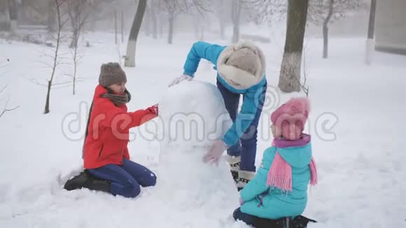 父母和孩子在雪地里玩耍妈妈和两个女儿在冬天堆雪人视频的预览图