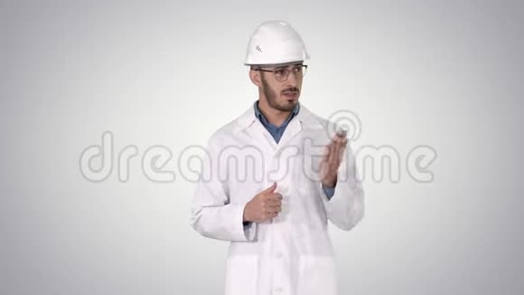 穿白色长袍和头盔的科学家用手指着侧面在渐变背景上向摄像机解释视频的预览图