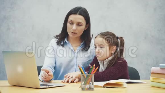 母亲和十几岁的女孩带着笔记本电脑一起在灰色背景上在这期间他们正在看手提电脑视频的预览图
