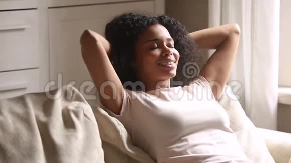 平静快乐的非裔美国年轻女性靠在沙发上放松视频的预览图
