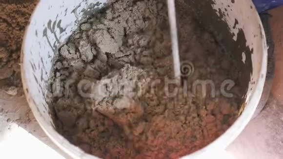 建筑工人用水和钻头搅拌混凝土在灰浆桶中封闭混合水泥视频的预览图