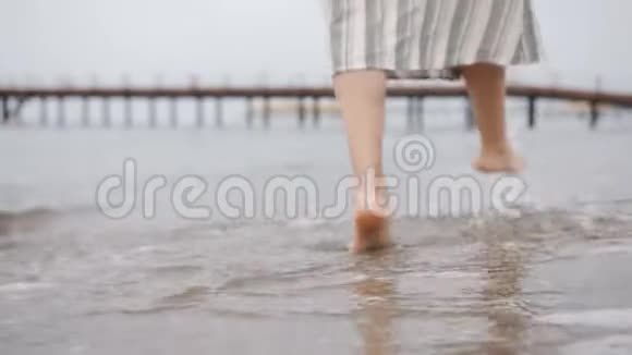 穿裙子的女人光着脚在海边特写双腿后视视频的预览图