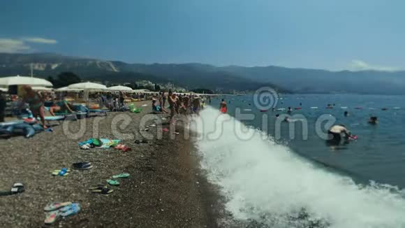 人们游客在度假小镇的鹅卵石海滩上放松炎热的夏天度假浪打岸上山区视频的预览图