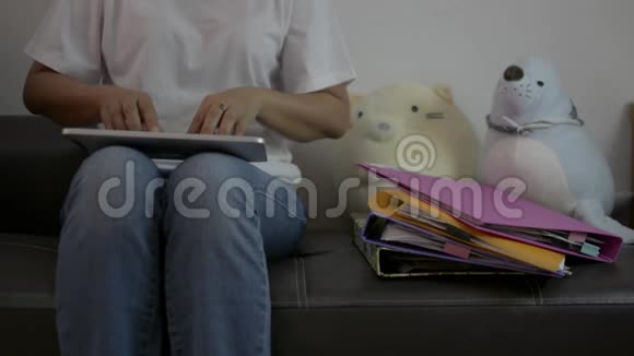 女士穿着休闲装坐在客厅的皮革沙发上使用数字平板电脑在家里做许多文件工作视频的预览图
