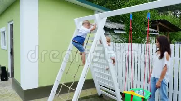 夏天在花园里孩子们一个四岁的男孩和一个一岁的女孩爬上孩子们楼梯视频的预览图