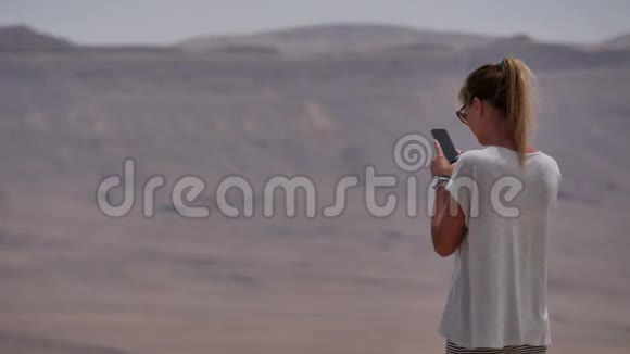 年轻女子在手机上拍摄沙漠火山口全景照片视频的预览图