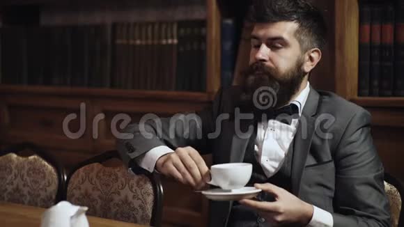可敬的人在书柜的背景上喝茶守旧的人拿着茶杯喝茶穿经典西装的男人视频的预览图