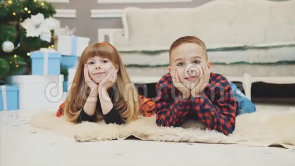 喜气洋洋的弟弟和妹妹正穿着红格子的衣服躺在毛毯上等待新年的到来视频的预览图