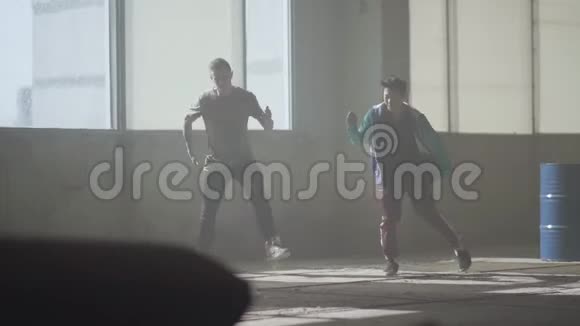 两个男孩在废弃建筑的大窗户前跳舞同时跳舞的青少年伙计们视频的预览图