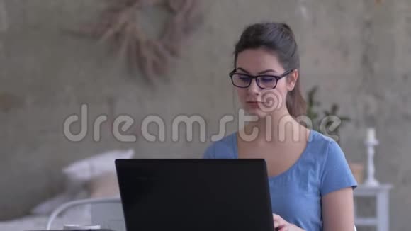 工作狂的女性戴眼镜在笔记本电脑键盘上输入文字在家做特写时看屏幕视频的预览图