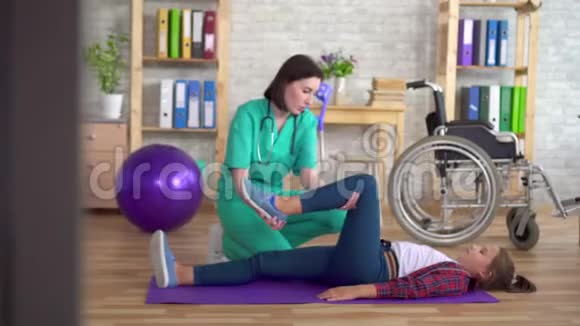 康复中心的物理治疗师帮助一个十几岁的女孩在康复后的腿部做热身运动视频的预览图