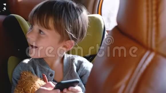 快乐兴奋的46岁白种人男孩微笑使用智能手机坐在汽车儿童安全座椅与玩具视频的预览图