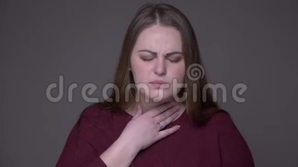 一位年轻的超重白种人女性的特写镜头一位患有疾病的咽喉咳嗽背景是灰色的视频的预览图