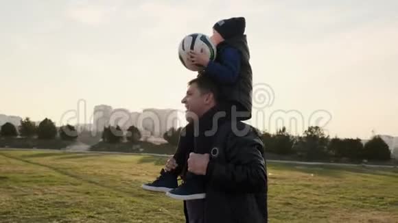 爸爸带着他的小儿子肩上扛着足球跟他玩慢动作视频的预览图