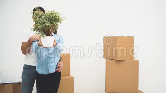 年轻夫妇一起搬到了一间新公寓他们拿着一个绿色的花盆微笑着动作动画4K视频的预览图